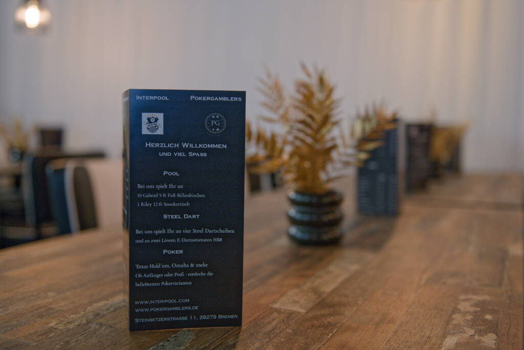 Nahaufnahme einer dunkelblauen Infokarte auf einem Holztisch in einem Billard- und Pokerlokal, im Hintergrund unscharfe Deko und weitere Karten