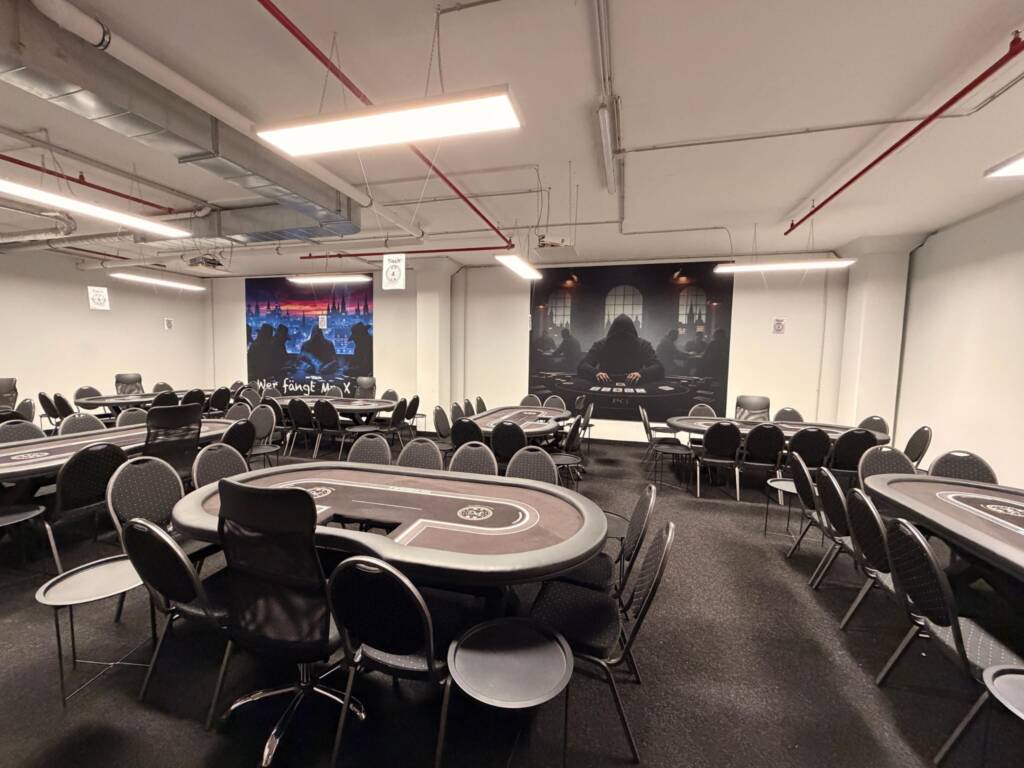 Halle mit diversen Pokertischen und großen Postern im Hintergrund
